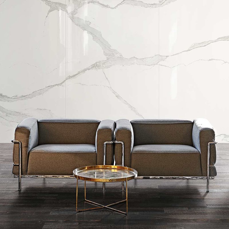Stylish gray upholstered armchairs with metal frames and a round coffee table, set against a marble wall background.